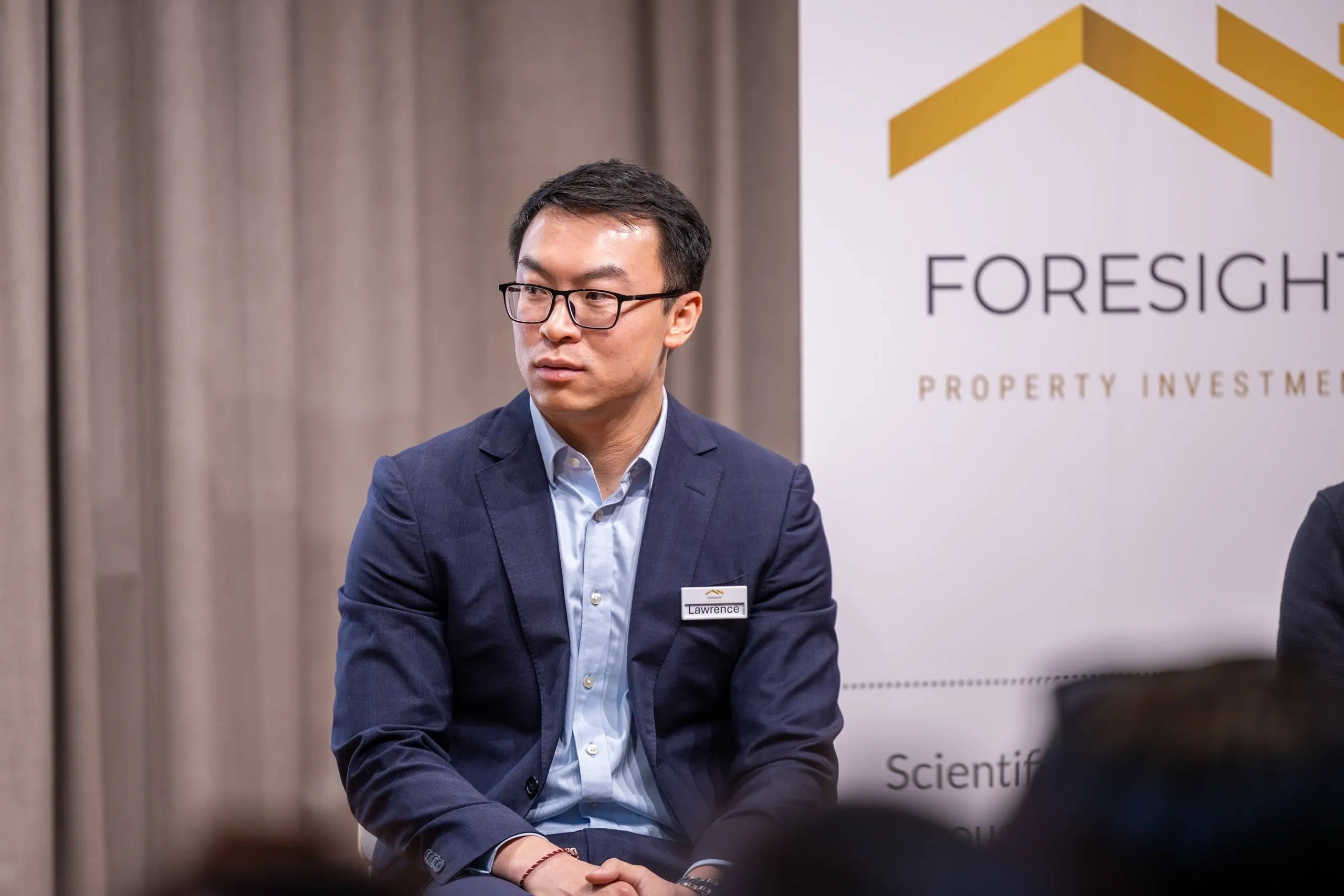 A man in a suit sitting and looking to the side at a professional event.