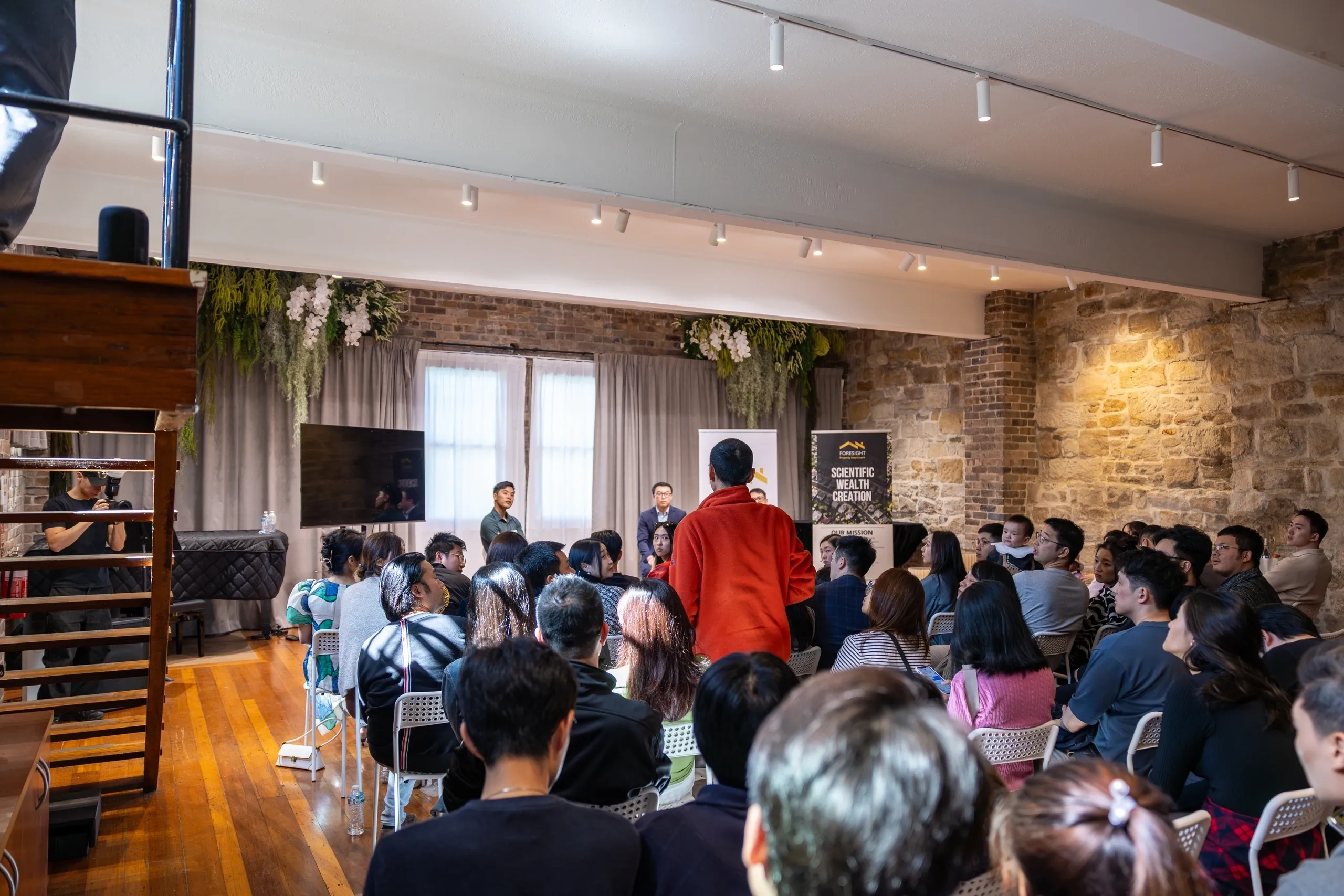 A person speaks to a seated audience in a cozy, well-lit room.