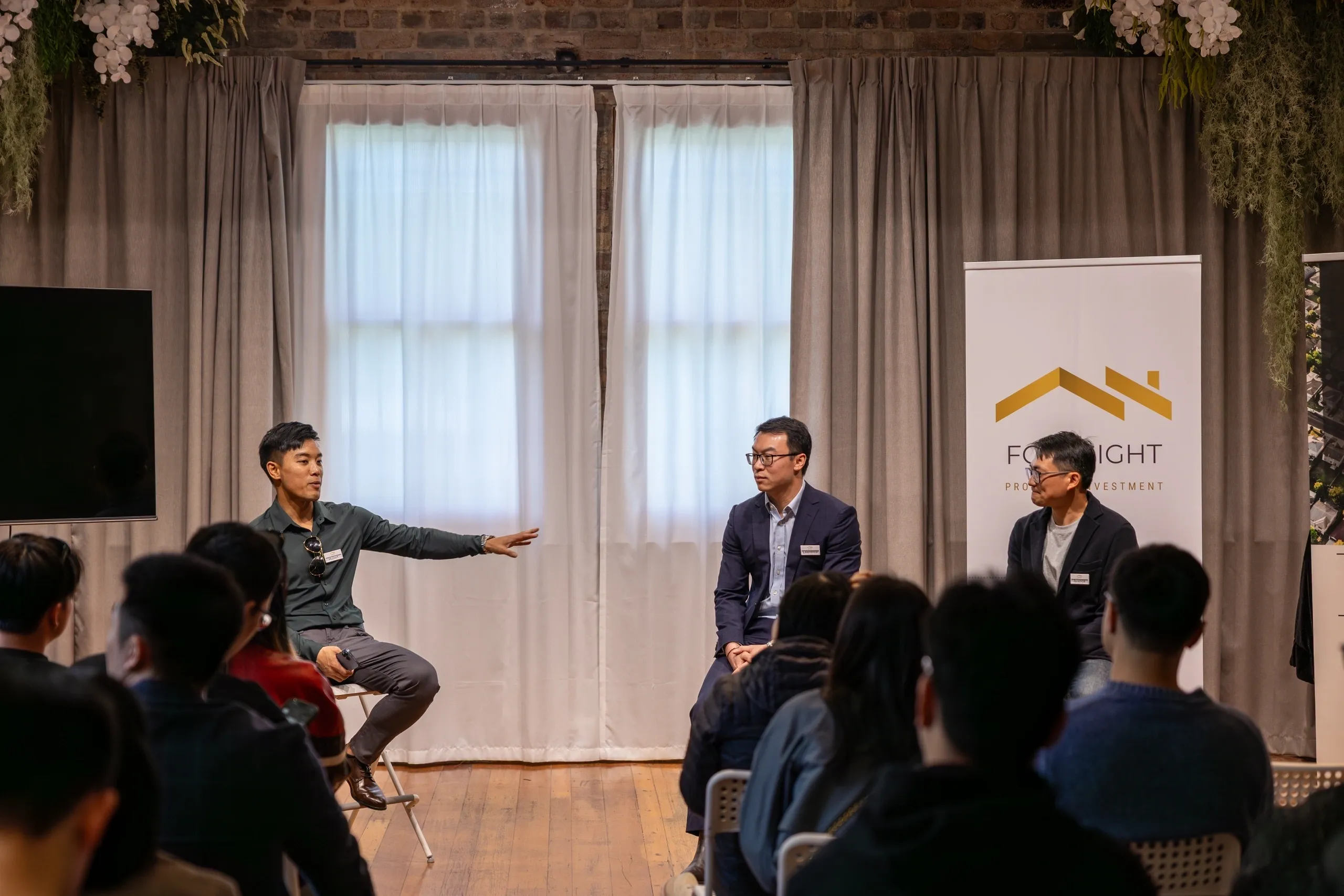 Three men in suits engage in a panel discussion in front of an audience.